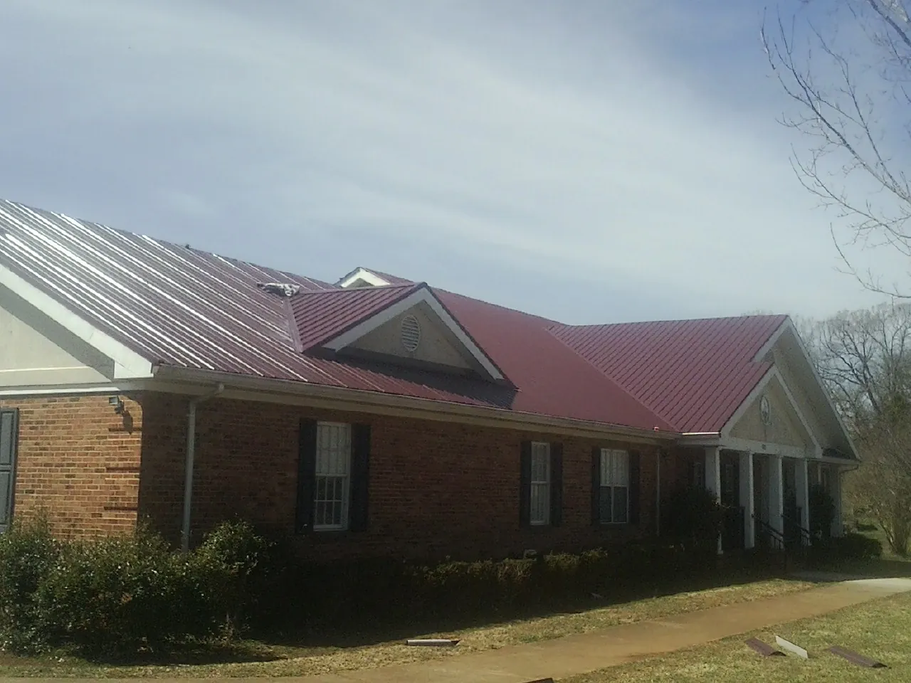 Red metal roof with gabled entries on a long brick building, from a Hail Damage Roof Repair job in Petersburg